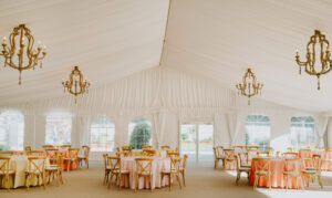 The Tent’s reception space set for a summer party with round tables decorated in sunset-inspired colors of orange, pink, and gold.