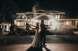 bride and groom pop champagne in front of wedding venue